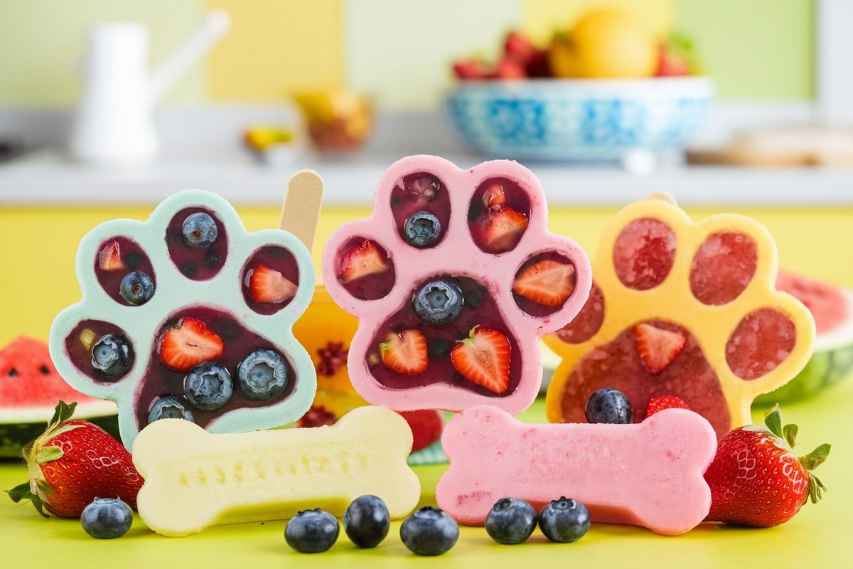 Close-up of colorful pawpsicles made with fresh fruits, shaped like paws and bones, on a bright kitchen countertop with a cheerful setting.